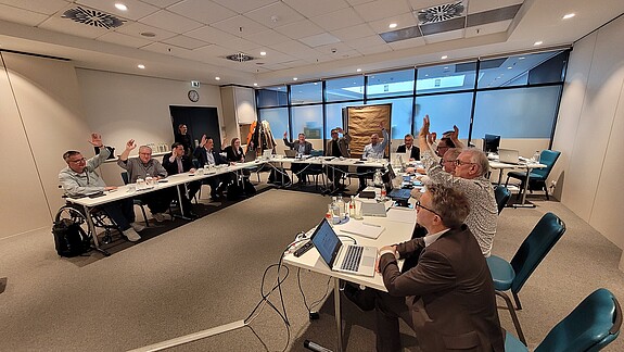 Abstimmung in einem Seminarraum. Alle heben die Hand.