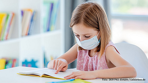 Schülerin liest Buch mit Maske in Klassenzimmer