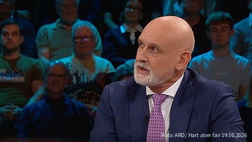 Ein Mann in Anzug sitzt an einem Tisch in einem TV-Studio und diskutiert