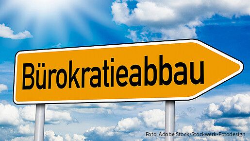 Gelbes, pfeilförmiges Straßenschild mit der Aufschrift „Bürokratieabbau“ vor blauem Himmel mit weißen Wolken. Das Schild zeigt nach rechts und symbolisiert den Weg zu weniger Bürokratie.