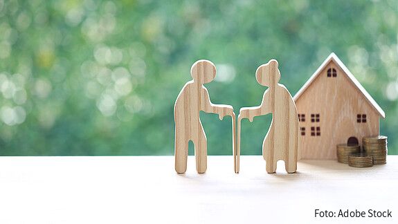 Rentenreform: nachhaltig und generationengerecht! Das Foto zeigt zwei kleine Holzfiguren, die ein Rentnerpaar darstellen. Im Hintergrund ein Haus, davor Münzen.