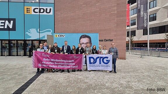 Eine Menschengruppe protestiert mit Bannern vor einem Konferenzzentrum
