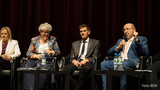 Vier Menschen sitzen auf einem Podium und diskutieren