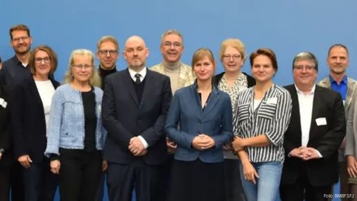 Eine große Gruppe Menschen steht vor einer hellblauen Wand und blickt in die Kamera.