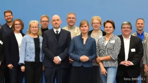 Eine große Gruppe Menschen steht vor einer hellblauen Wand und blickt in die Kamera.