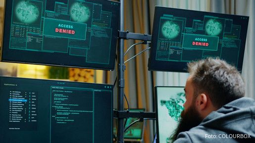 Ein Mann sitzt vor mehreren Computer-Monitoren, auf denen "Zugriff verweigert" zu lesen ist.