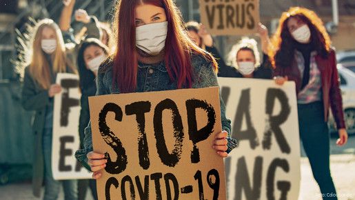 Auf einer Demonstration halten Frauen mit Minde-Nasen-Schutz Plakate mit der Aufschrift "Stop Covid-19"