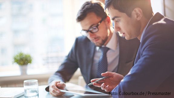 Zwei Männer im Büro sehen gemeinsam auf Tablet und besprechen sich