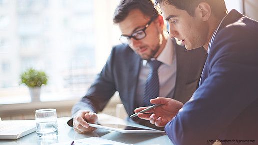 Zwei Männer im Büro sehen gemeinsam auf Tablet und besprechen sich