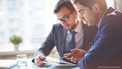 Zwei Männer im Büro sehen gemeinsam auf Tablet und besprechen sich
