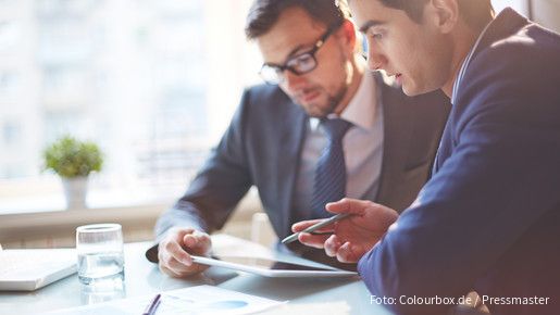 Zwei Männer im Büro sehen gemeinsam auf Tablet und besprechen sich