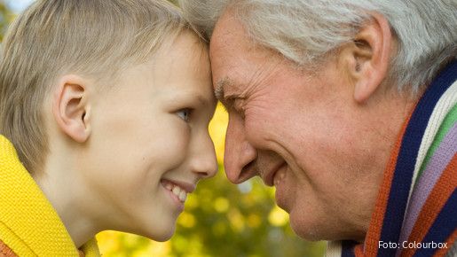 Großvater und Enkelsohn lehnen die Köpfe aneinander und lächeln sich gegenseitig an. 