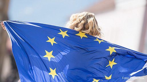 Das Foto zeigt ein Mädchen, das eine EU-Fahne als Umgang nutzt. Die Sterne sind zu erkennen, über dem Rand der Fahne ihre Haare.