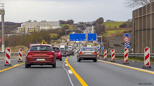 Zu sehen sind Autos auf einer Autobahn, rechts und links am Fahrbahnrand stehen Baustellen-Barken.