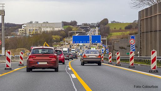 Zu sehen sind Autos auf einer Autobahn, rechts und links am Fahrbahnrand stehen Baustellen-Barken.