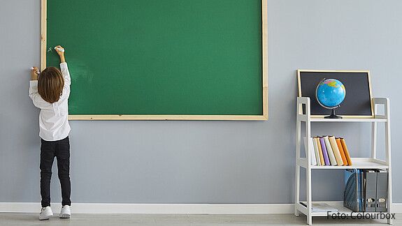 Daten für Weiterentwicklung der Bildung nutzen, aber mit klaren Regeln Das foto zeigt ein Kind, das eine Tafel beschriftet. Rechts ist ein Regal mit einem Globus zu sehen.