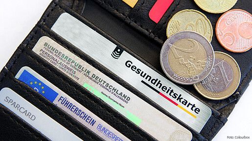 Das Bild zeigt eine Geldbörse mit einer Gesundheitskarte, Ausweisdokumenten und Münzen.