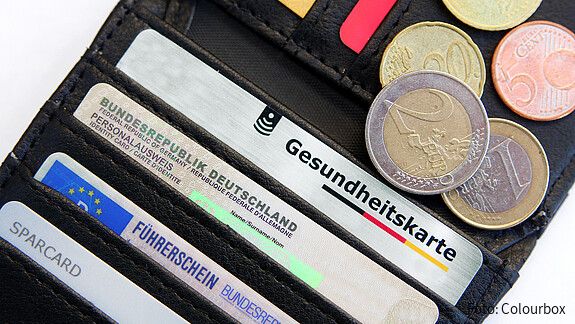 Das Bild zeigt eine Geldbörse mit einer Gesundheitskarte, Ausweisdokumenten und Münzen.