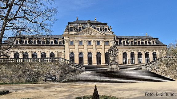 Ein barocker Palast mit blauem Himmel im Hintergrund und einer Parkanlage im Vordergrund