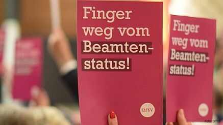 Eine Gruppe Menschen hält Schilder mit der Aufschrift "Finger weg vom Beamtenstatus" hoch