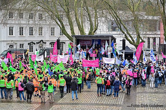 Eine Menschengruppe protestiert mit bunten Fahnen auf einem öffentlichen Platz.