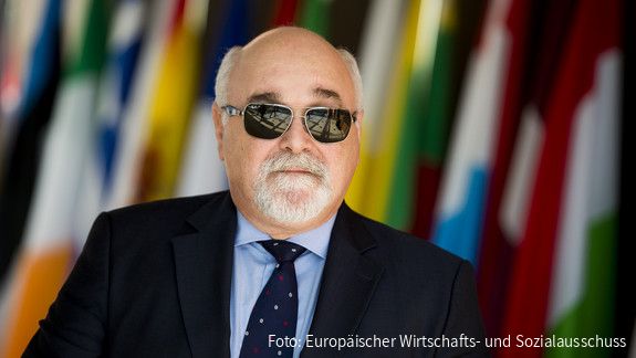 Ioannis Vardakastanis im Portrait, im Hintergrund Fahnen der EU-Mitgliedstaaten