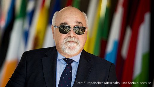 Ioannis Vardakastanis im Portrait, im Hintergrund Fahnen der EU-Mitgliedstaaten