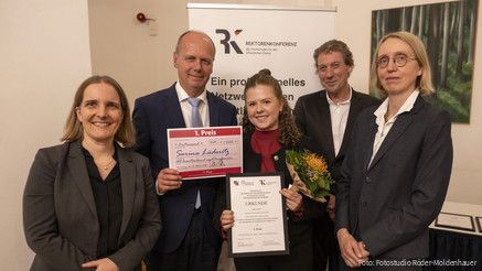 Fünf Menschen halten eine Urkunde für den ersten Platz und blicken in die Kamera