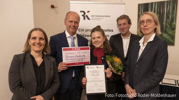 Fünf Menschen halten eine Urkunde für den ersten Platz und blicken in die Kamera