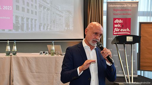 Ein Mann steht vor einer Leinwand mit einem Mikrofon in der Hand 