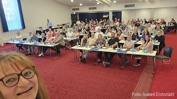 Selfie einer Seminarleiterin mit dem vollen Seminarraum im Hintergrund