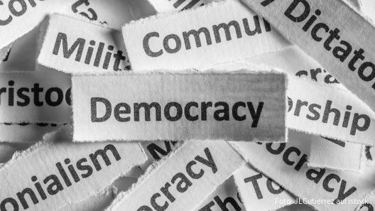 Verschiedene Staatsformen sind auf Zettel geschrieben, die Demokratie liegt über allen
