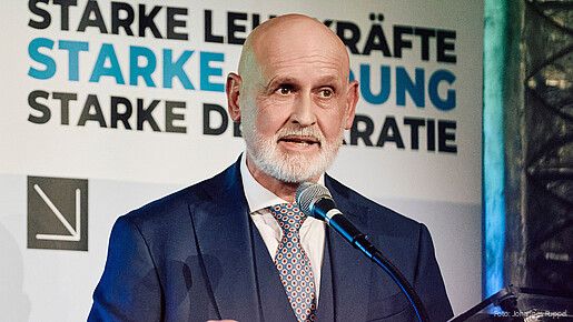 Herr Geyer steht hinter einem Rednerpult und spricht in das Mikrofon