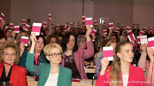 Frauen sitzen in einem großen Konferenzraum und halten Abstimmungskarten in die Luft