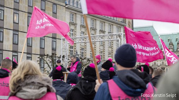 Demonstreierende in pinken Warnwesten stehen vor einer Bühne, auf der Thomas Treff in ein Mikrofon spricht