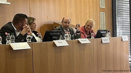 Vier Frauen und zwei Männer sitzen an einem Konferenztisch und diskutieren miteinander