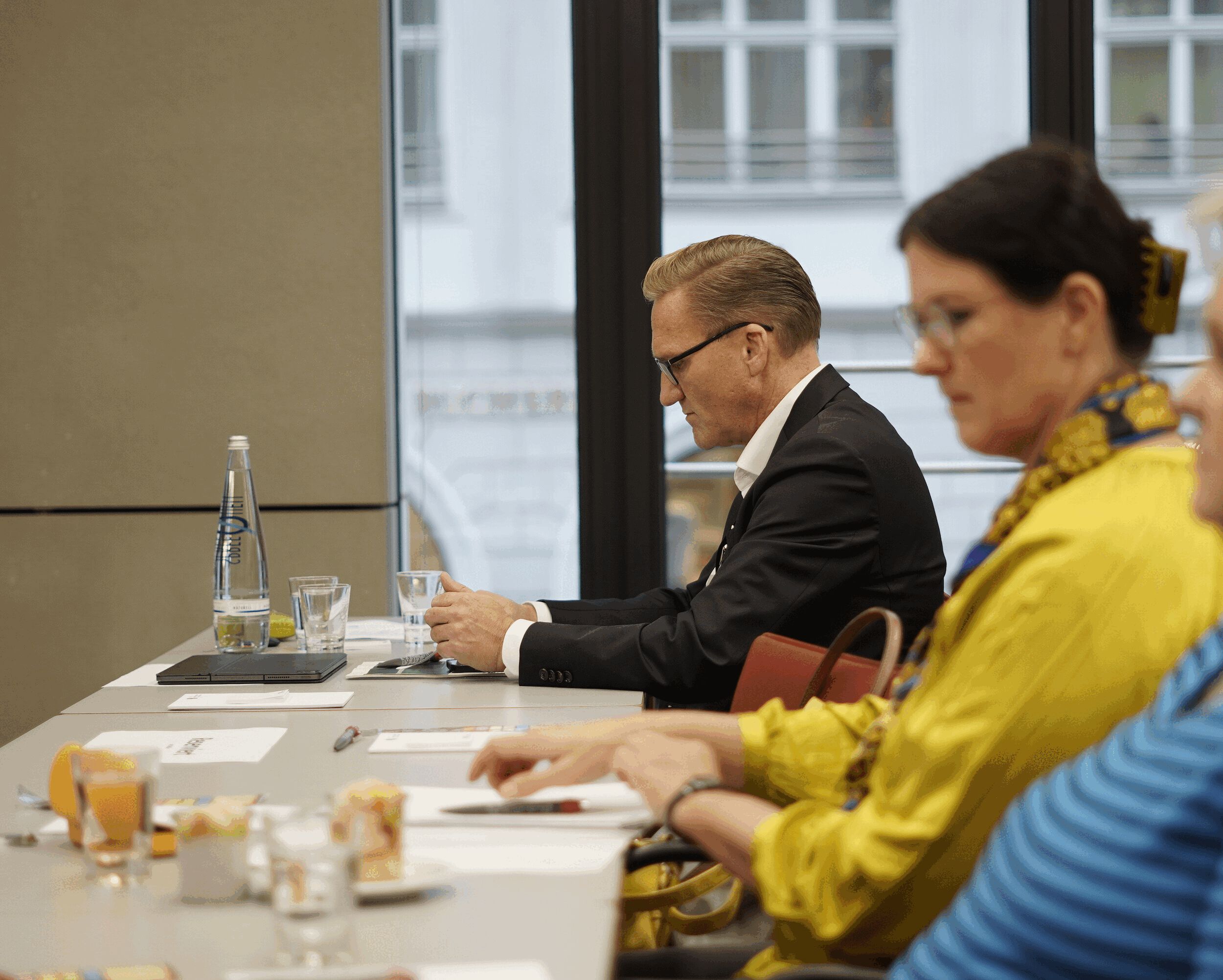 Drei Menschen sitzen in einem Seminarraum an einem Tisch