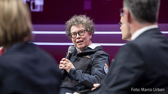 Eine Frau sitzt auf der Bühne und diskutiert mit anderen Teilnehmern. Es handelt sich um Sabine Lackner, THW-Präsidentin