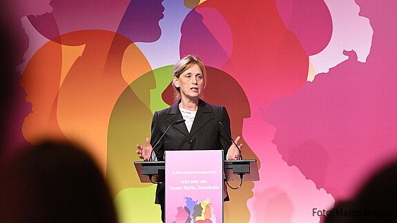 Eine Frau steht hinter einem Rednerpult und spricht in das Mikrofon. Es handelt sich um Bundesfamilienministerin Karin Prien. 