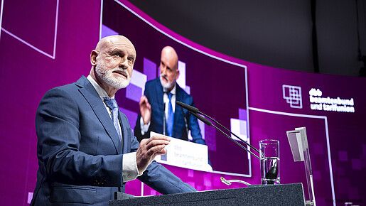 Ein Mann steht auf einer Bühne hinter einem Rednerpult und spricht in ein Mikrofon. 