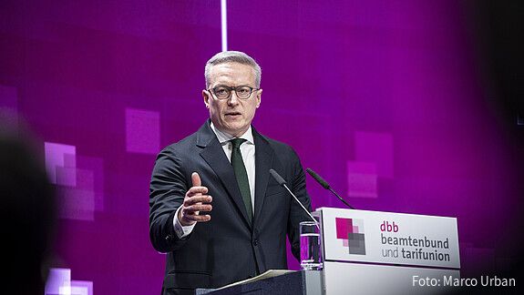 Ein Mann steht auf einer Bühne hinter einem Rednerpult und spricht in ein Mikrofon. Es handelt sich um Karsten Wildberger, Bundesminister für Digitales und Staatsmodernisierung