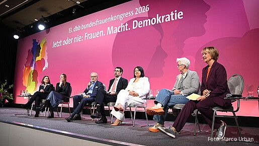 Menschen sitzen auf Stühlen auf einer Bühne und diskutieren miteinander. 