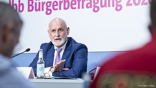 Ein Mann in Anzug sitzt hinter einem Tisch und spricht in ein Mikrofon.