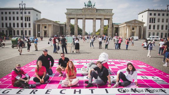 Tag der Deutschen Einheit Junge Menschen sitzen vor dem Brandenburger Tor in Berlin auf einem überdimensionierten Scrabble-Spielfeld, auf dem das Wort Gerechtigkeit steht