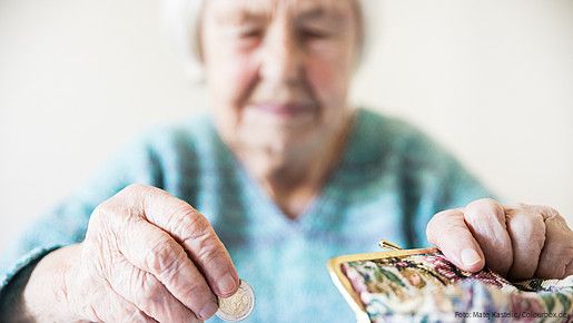 Eine unglücklich wirkende Seniorin zählt am Tisch die wenigen Münzen ihre Pension.