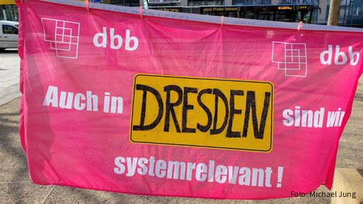 Ein Banner wird in die Kamera gehalten, auf dem steht "Auch in Dresden sind wir systemrelevant.""