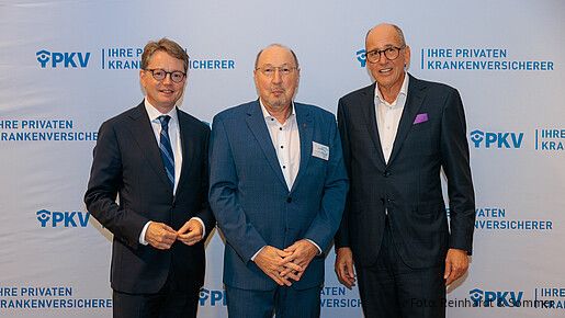 Drei Männer in Anzügen stehen vor einer weißen Leinwand mit PKV-Logos und blicken in die Kamera