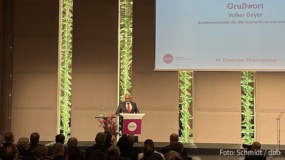 Ein Mann steht auf einer großen Bühner hinter einem Rednerpult und hält eine Rede