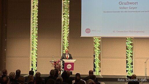 Ein Mann steht auf einer großen Bühner hinter einem Rednerpult und hält eine Rede