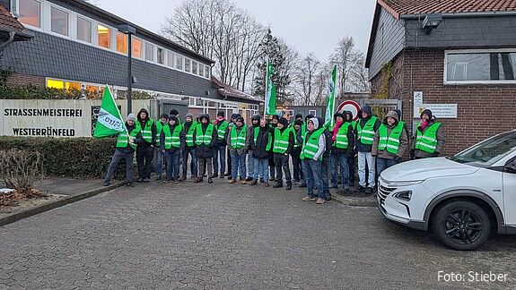 Eine Gruppe Menschen in grünen Warnwesten protestiert vor einem Gebäude
